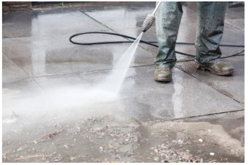 Jet washing a concrete driveway with a jet wash and a mans feet showing